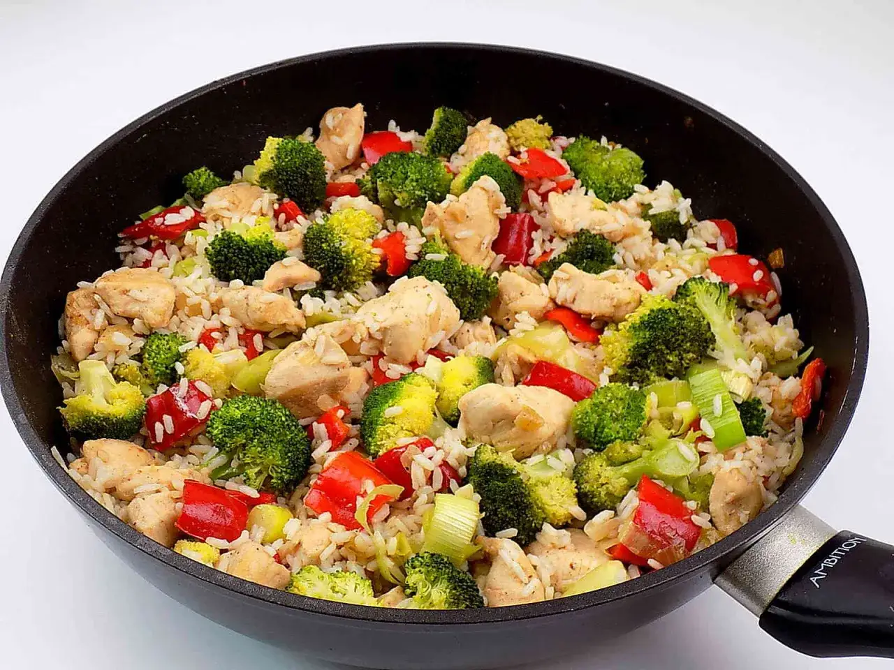 Ryż z warzywami i kurczakiem w sosie, danie pełne kolorów i smaku, przygotowane na patelni.