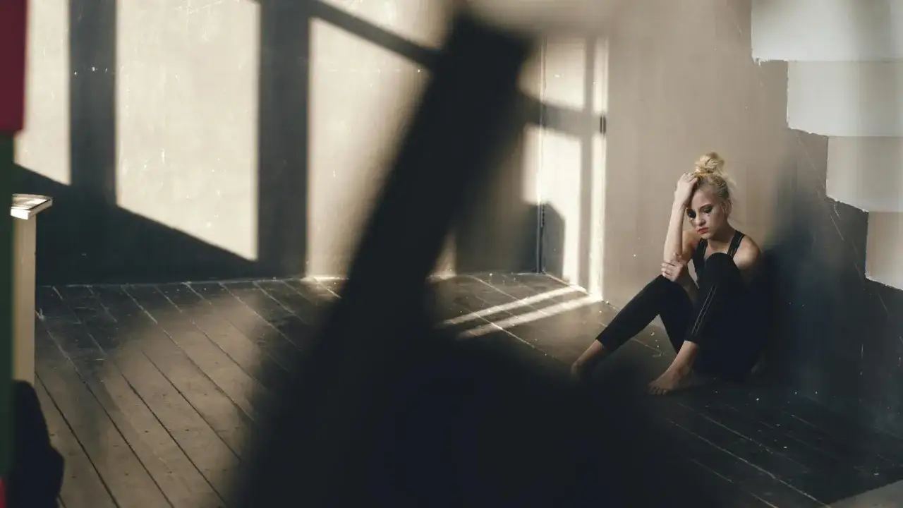 Smutna dziewczyna siedzi na podłodze w pustym pokoju, z rozmazanym makijażem. Cienie okien padają na ściany i podłogę. To uczucie, gdy na Tinderze brak par.