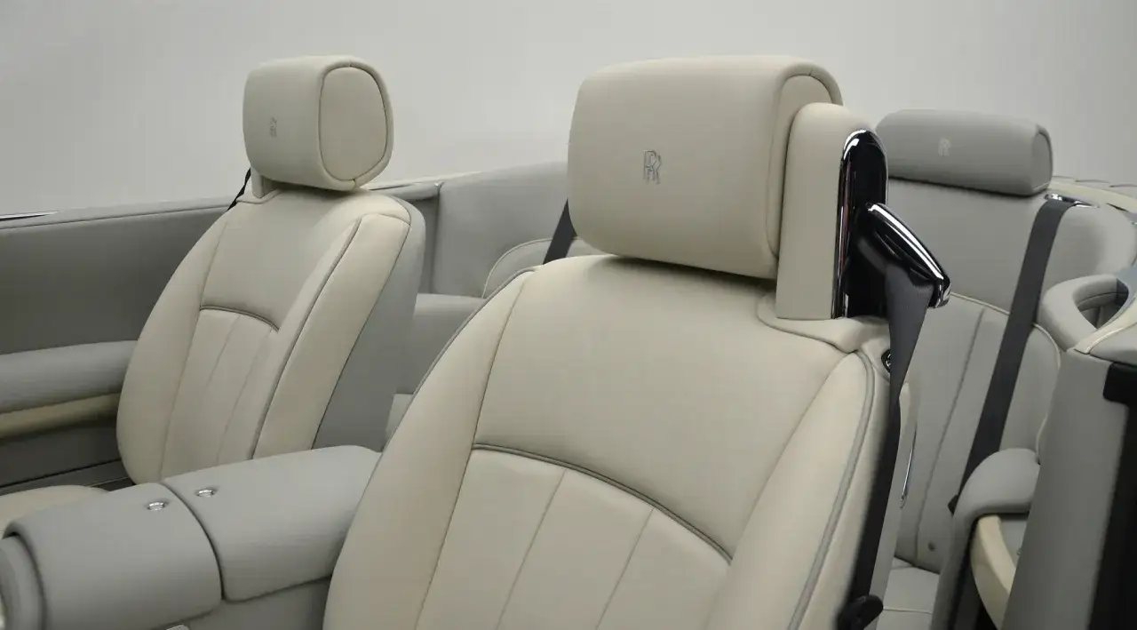Jasne, kremowe wnętrze Rolls-Royce Phantom Drophead Coupe z dyskretnym logo marki na zagłówkach.
