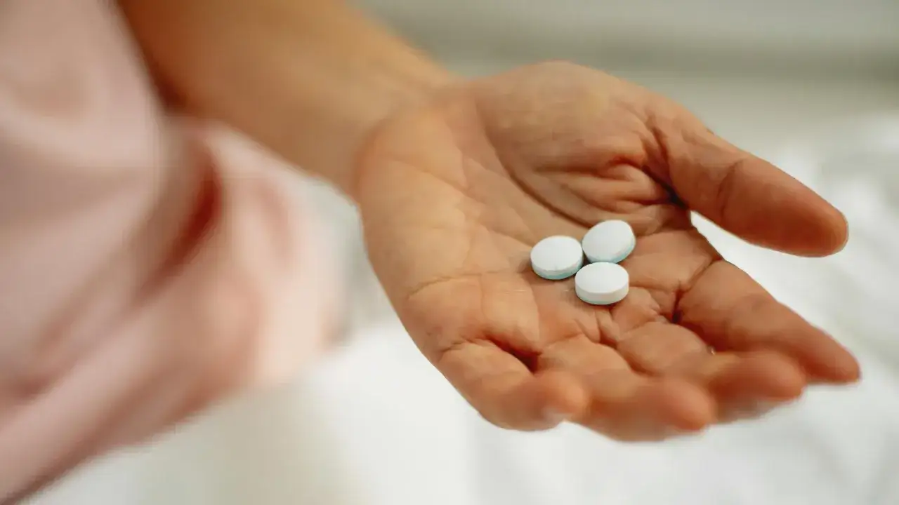 Dłoń trzyma trzy białe tabletki. To niesteroidowe leki przeciwzapalne, kt&oacute;re mogą przynieść ulgę w b&oacute;lu.
