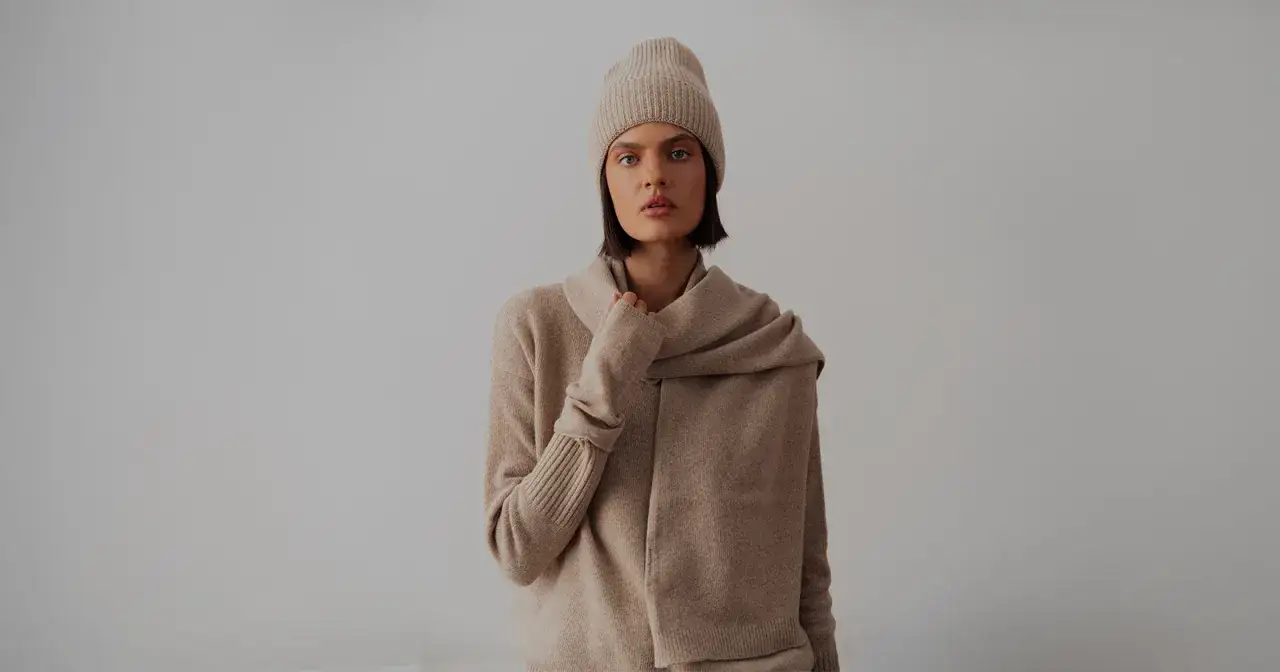 Kobieta w beżowym swetrze, czapce i szalu. Delikatna tkanina sugeruje, jak rozpoznać kaszmir &ndash; miękkość i lekkość.