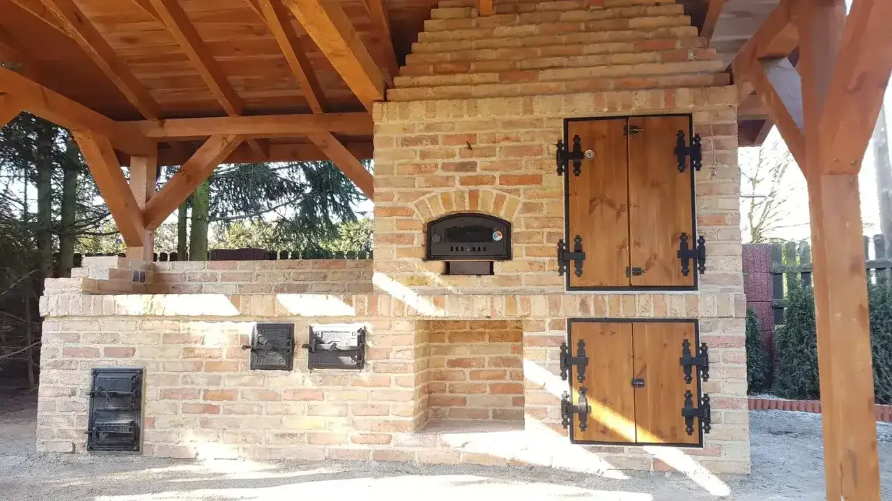 Solidny grill z wędzarnią z cegły, z drewnianym zadaszeniem i drzwiczkami. Idealny do letnich przyjęć.