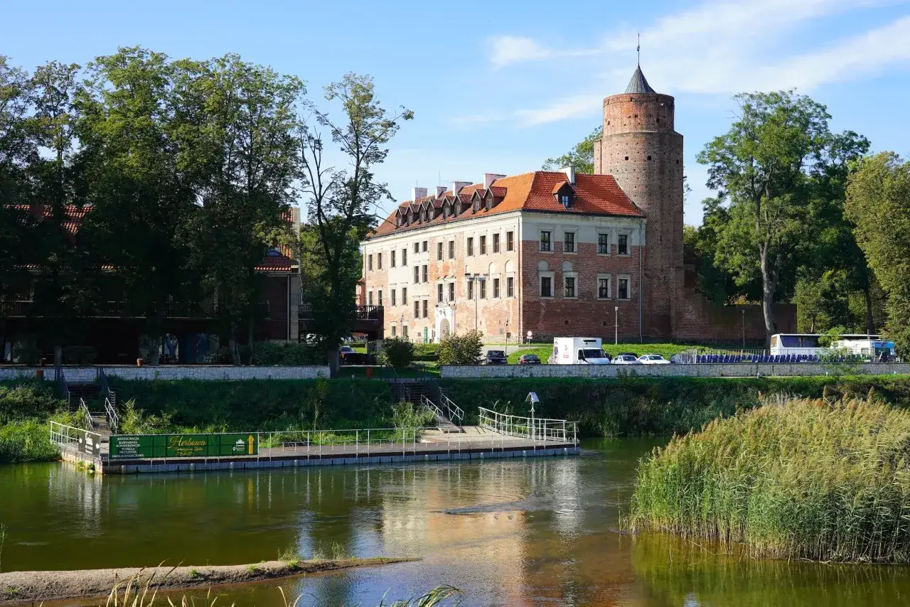 Zamek w Uniejowie, gdzie znajduje się urokliwy zamek z wieżą, otoczony zielenią i rzeką.