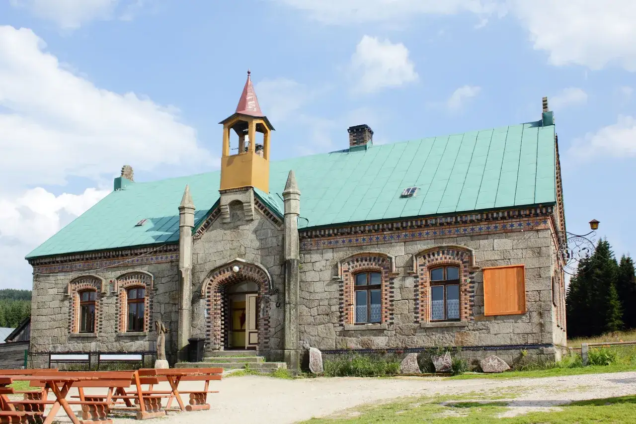 Kamienna stacja turystyczna Orle z zielonym dachem i wieżyczką. Przed budynkiem stoją drewniane ławy i stoły.