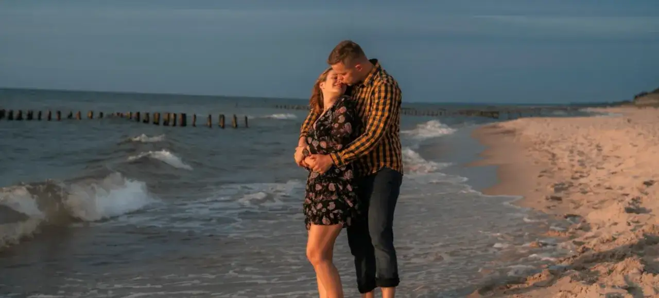 Para zakochanych cieszy się romantycznym weekendem dla dwojga nad morzem all inclusive. Delikatne fale obmywają ich stopy na piaszczystej plaży.