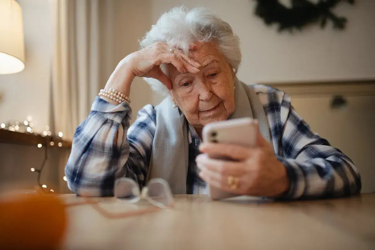 Starsza pani zamyślona, trzymająca telefon. To właśnie co to senior &ndash; osoba pełna doświadczeń, korzystająca z technologii.