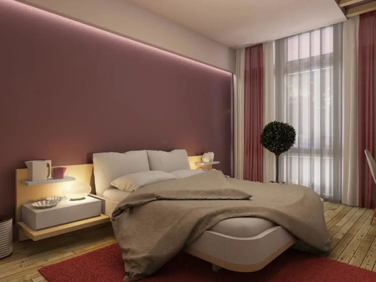 Elegancka sypialnia z łóżkiem, nocnymi stolikami i subtelnym oświetleniem. Listwa LED na ścianie tworzy nastrojową atmosferę.
