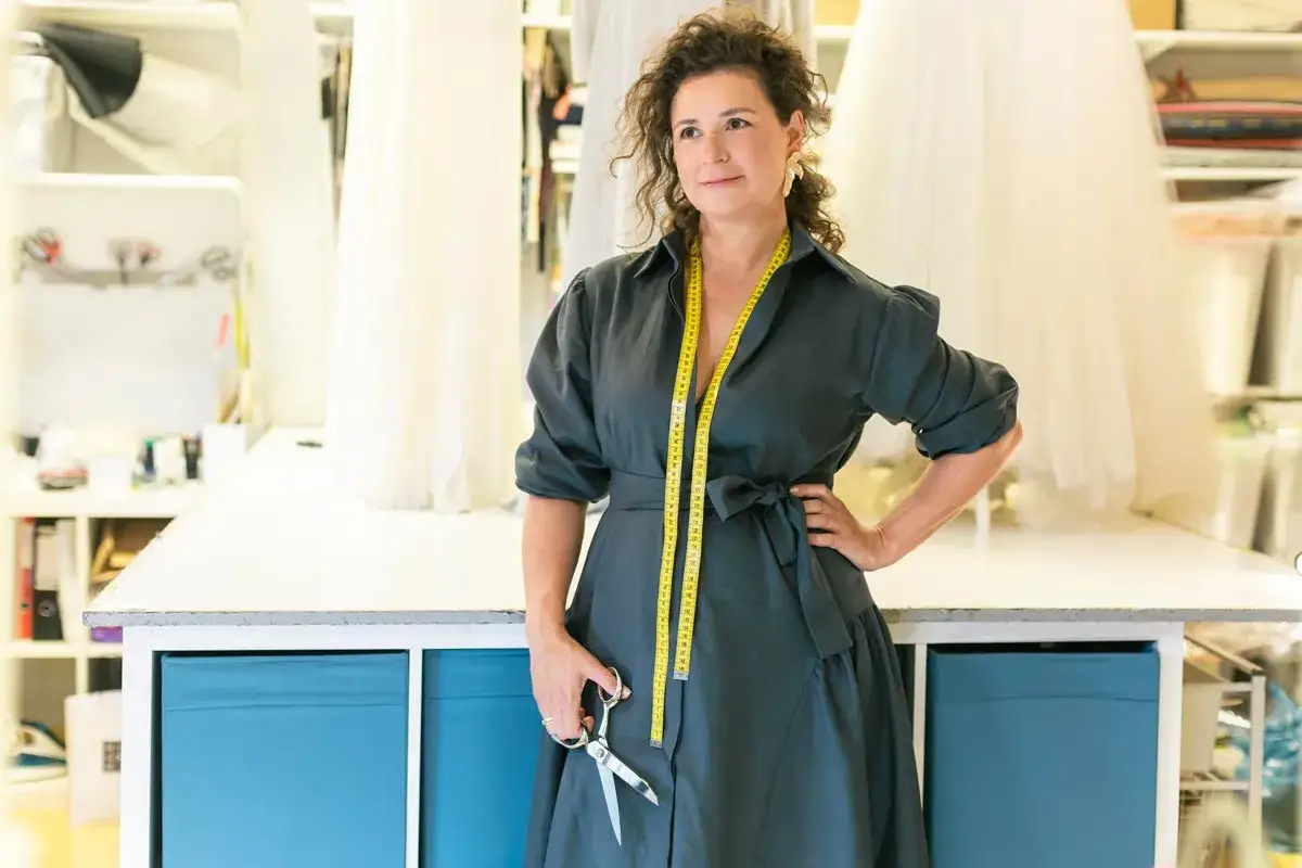 Krawcowa z miarką i nożyczkami w pracowni, gotowa pokazać, jak uszyć sukienkę.