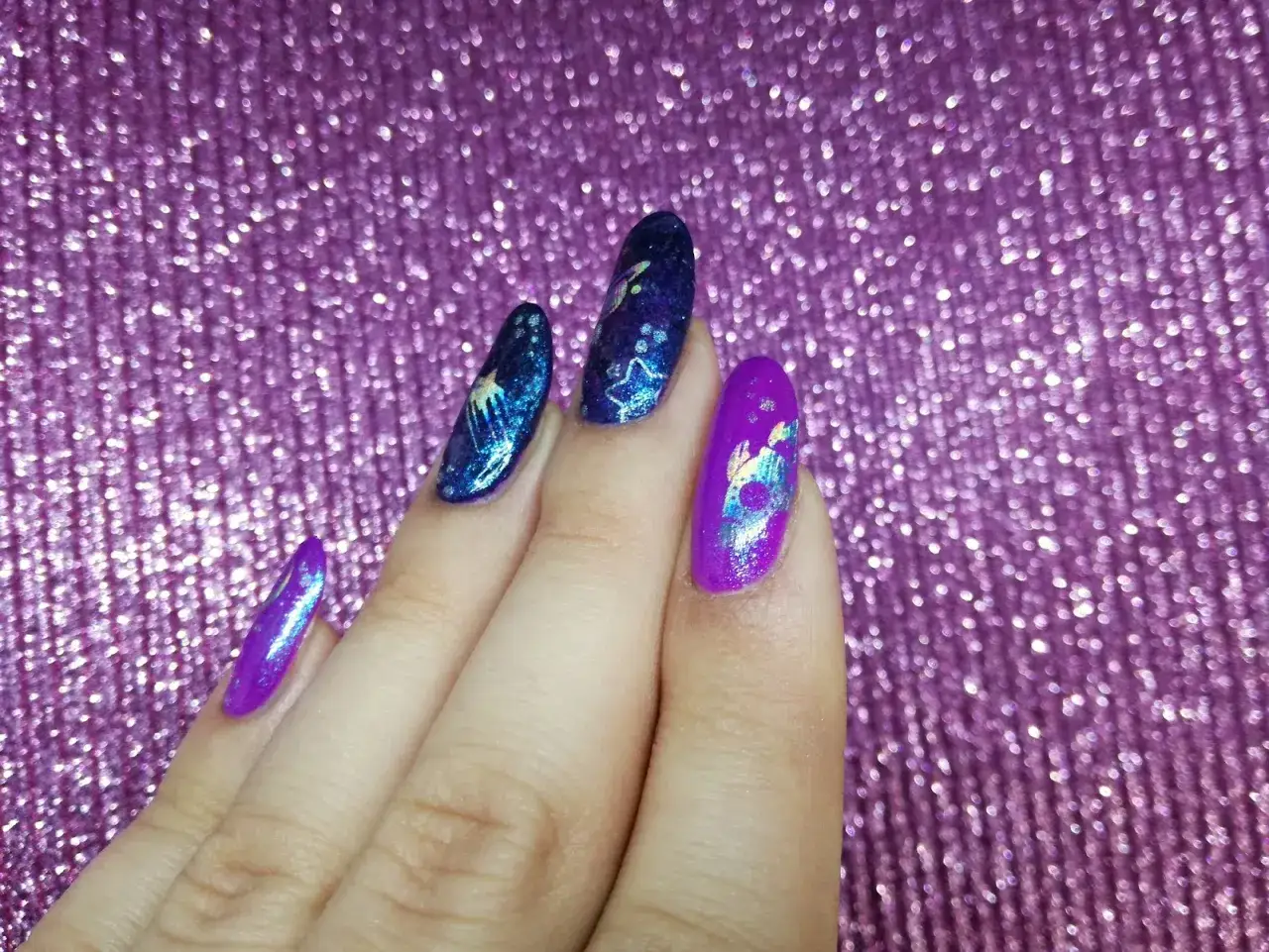 Paznokcie z folią transferową w odcieniach fioletu i granatu, zdobione motywami kosmicznymi.