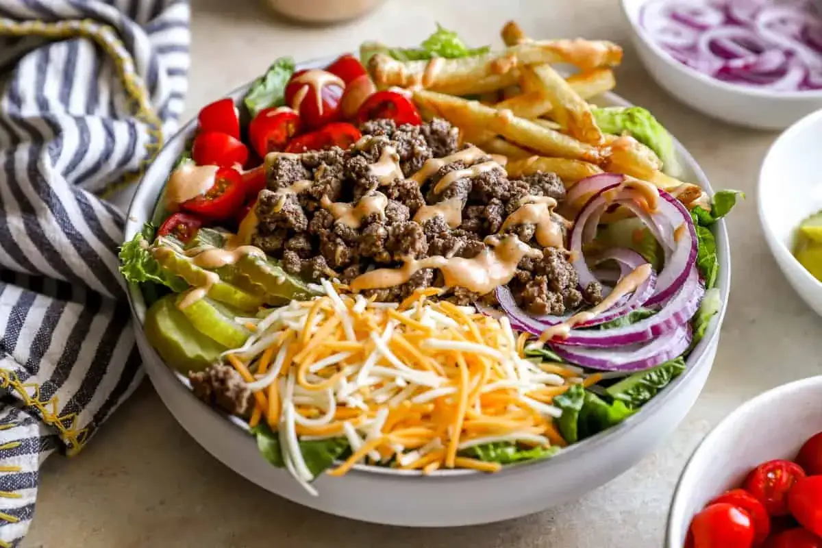 Pyszna sałatka big mac z mielonym mięsem, frytkami, serem, pomidorkami i sosem.