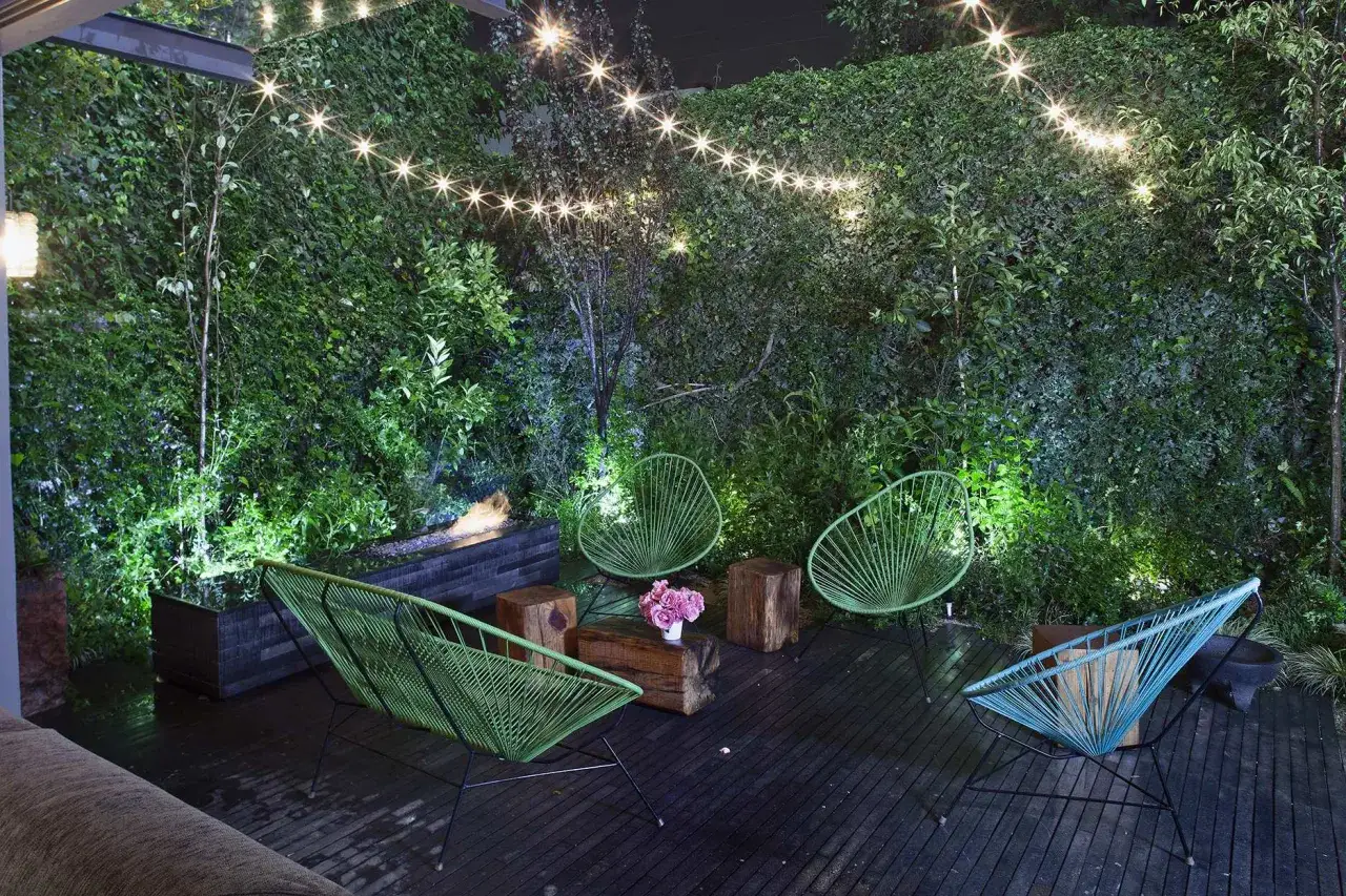 Oświetlenie tarasu inspiracje: zielona ściana roślin, wiszące lampki i nowoczesne fotele tworzą magiczny klimat.