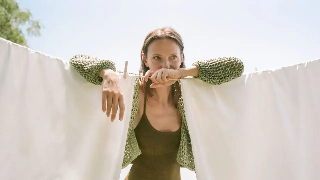 Kobieta w zielonym swetrze z tencelu wiesza pranie. Tencel to ekologiczna tkanina.