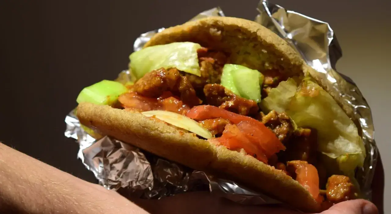 Pyszny kebab bez glutenu w bułce z mięsem, warzywami i sosem, zawinięty w folię aluminiową.