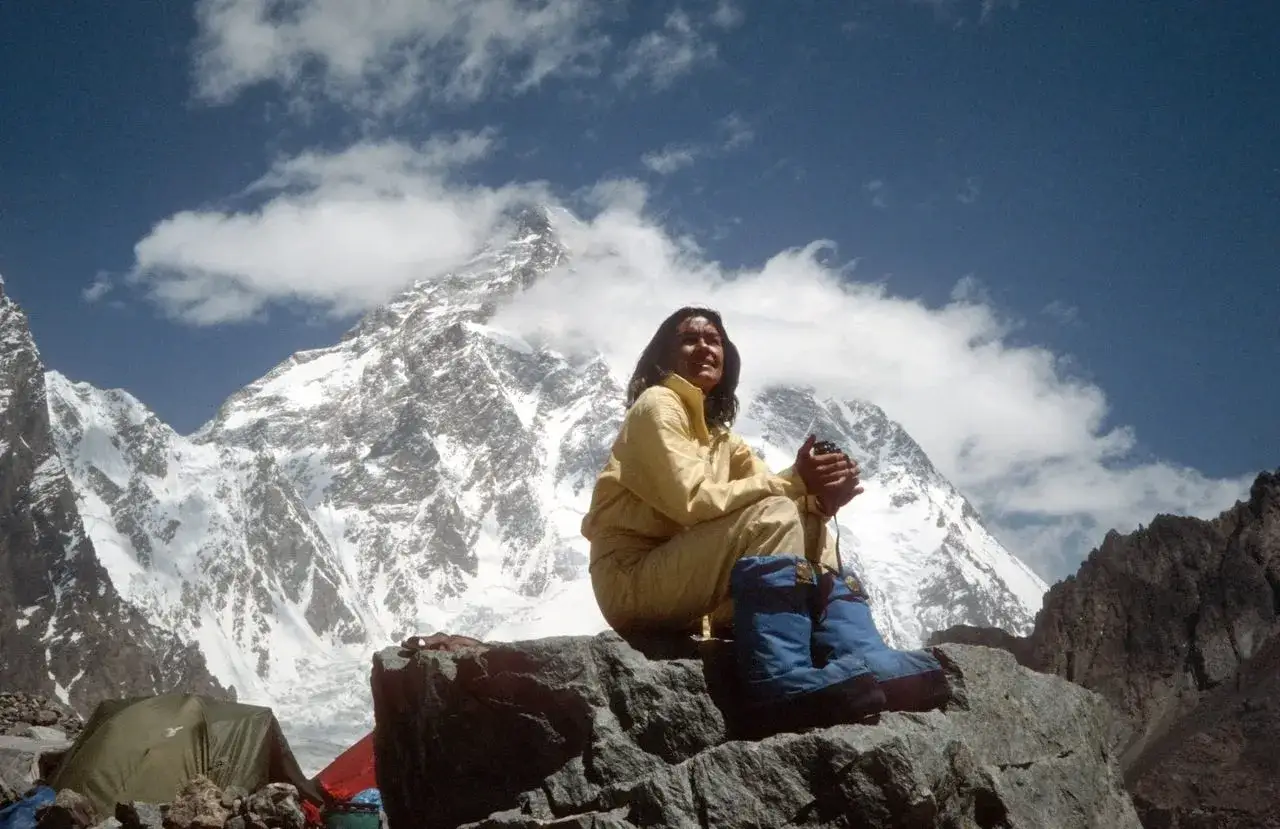 Kobieta w ż&oacute;łtym kombinezonie siedzi na skale, w tle ośnieżone g&oacute;ry. Inspiracja do lektury książek o wspinaczce.