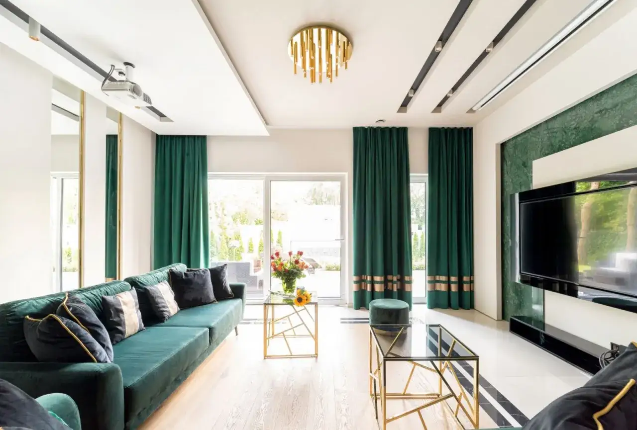 Eleganckie, zielone zasłony z ozdobnymi pasami idealnie komponują się z głęboką zielenią kanapy, tworząc luksusową aranżację salonu.