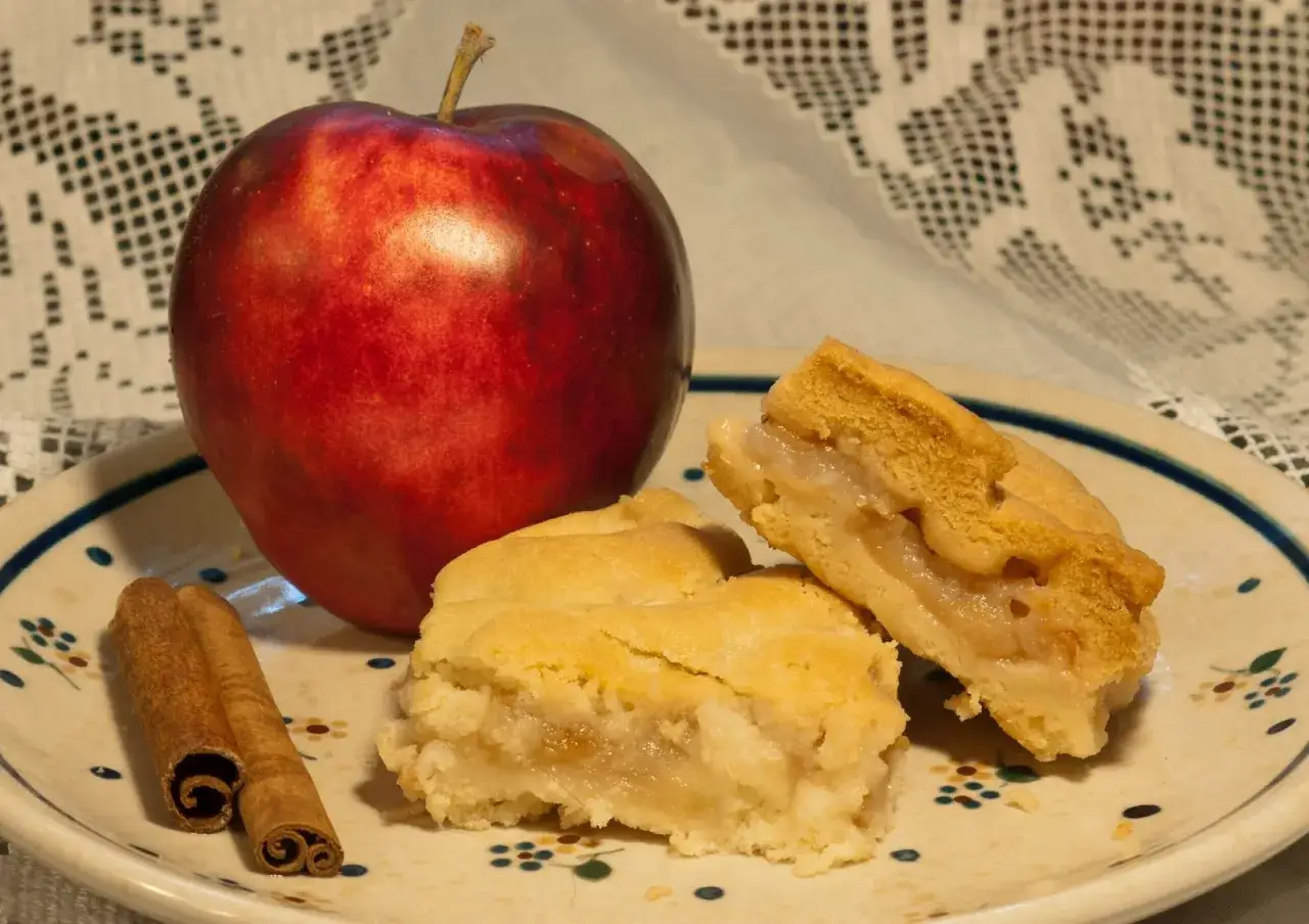 Jabłko, laska cynamonu i kawałki szarlotki na talerzu. Zastanawiasz się, ile czasu piec szarlotkę, by była tak pyszna?