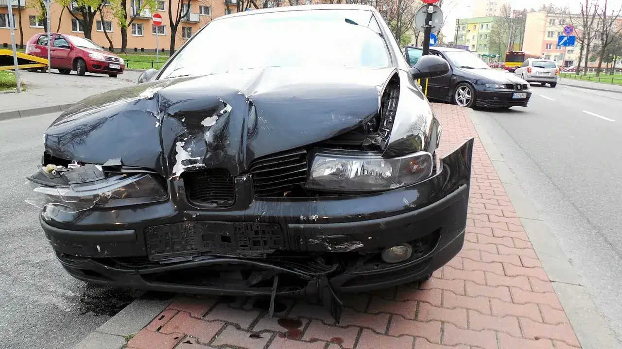 Zarysowanie auta w leasingu: przód czarnego samochodu jest mocno zniszczony po wypadku, z pogiętą maską i rozbitą lampą.