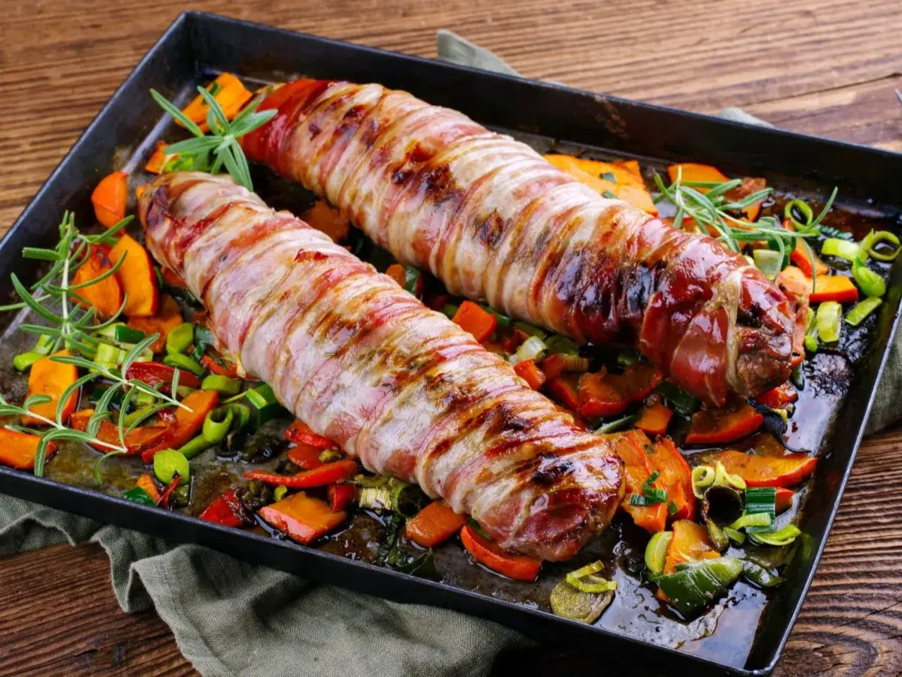 Dwie poledwiczki wieprzowe zawinięte w boczek, pieczone z warzywami. Idealny pomysł, jak przyrzadzic poledwiczke wieprzowa na obiad.