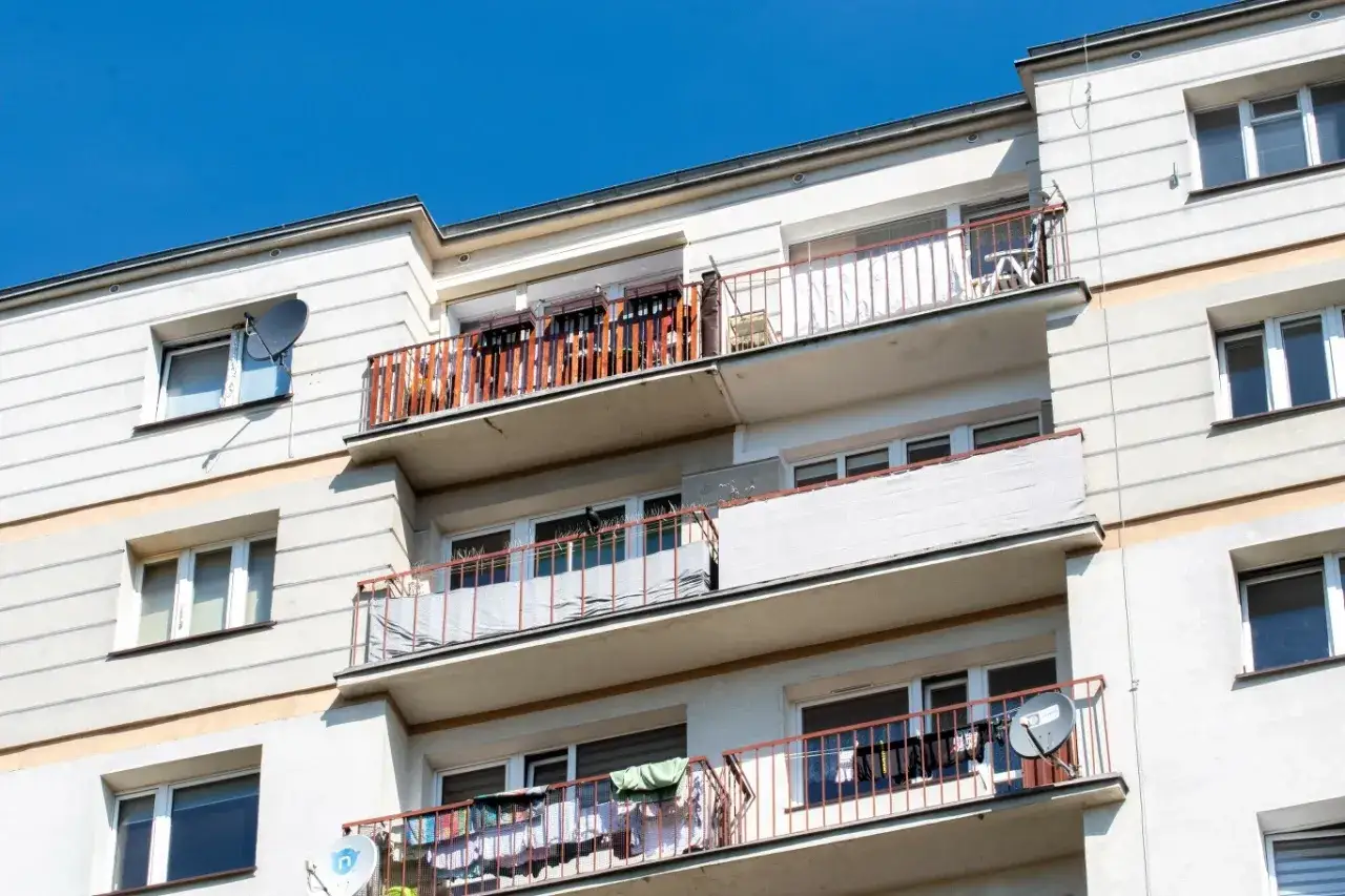 Wielopiętrowy blok z balkonami, na których suszy się pranie. Czy balkon to część wspólna? Widać anteny satelitarne.