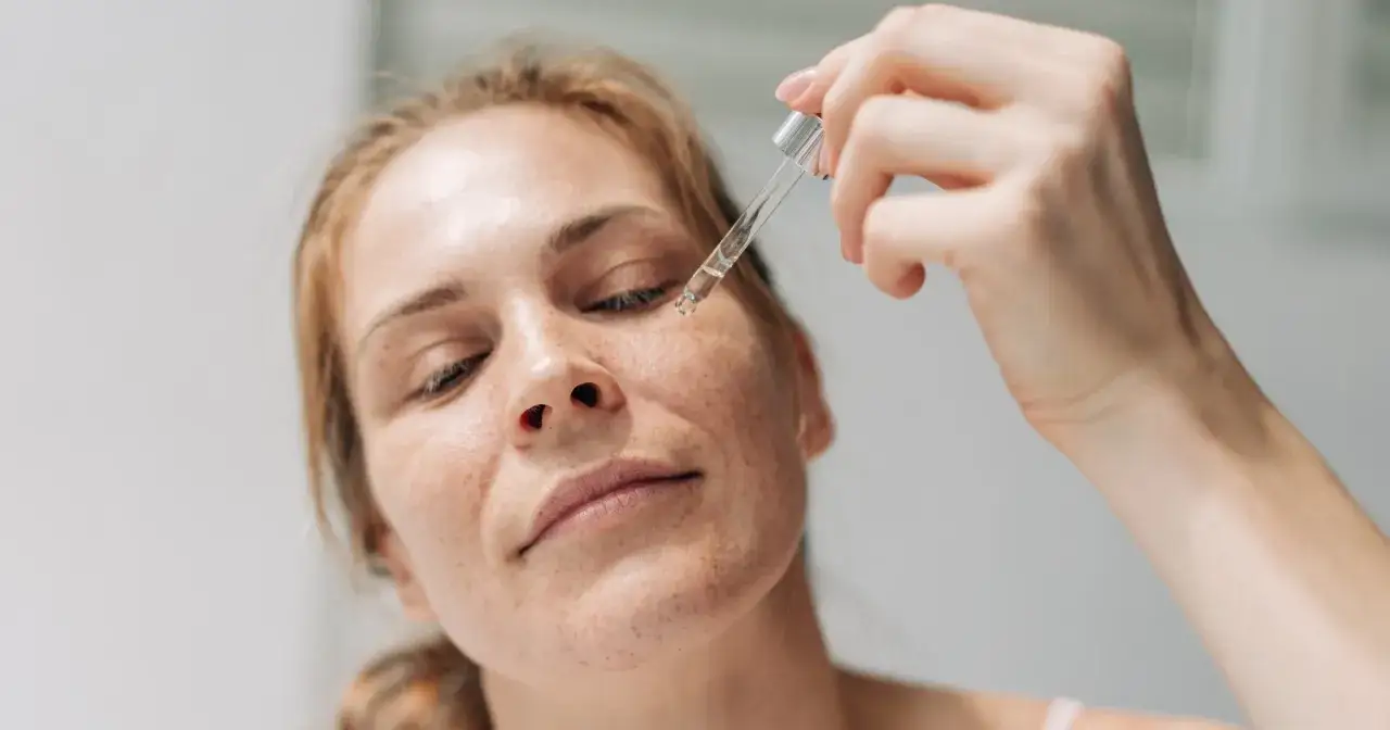 Kobieta aplikuje serum z pipetką na twarz. Nawet latem można stosować retinol, pamiętając o ochronie przeciwsłonecznej.