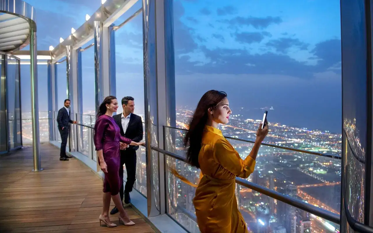 Elegancka para podziwia nocną panoramę Dubaju, a kobieta robi zdjęcie. Bilety na Burdż Chalifa to klucz do tej niesamowitej perspektywy.