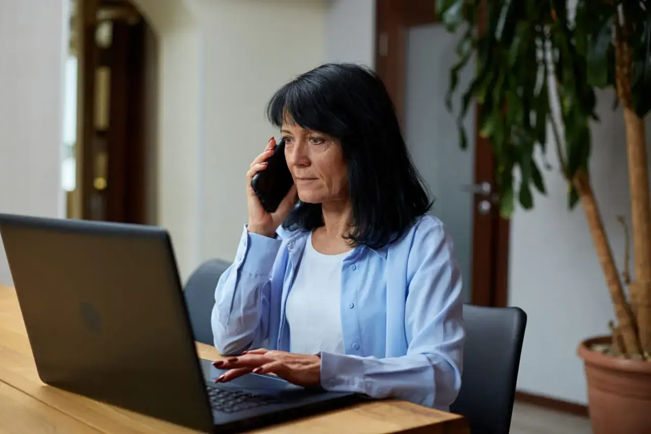 Kobieta przez telefon sprawdza, jak sprawdzić numer w kolejce do sanatorium, siedząc przy laptopie.