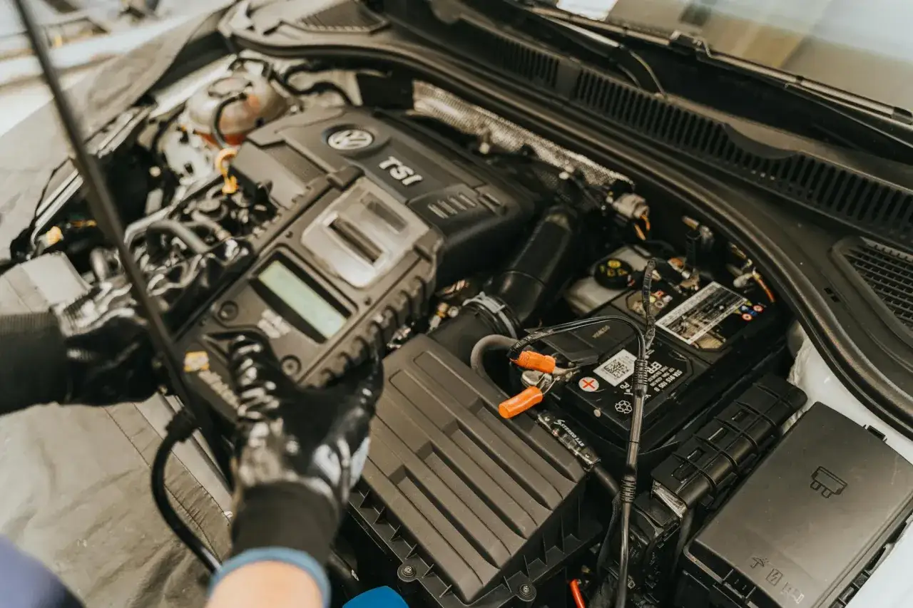 Mechanik diagnozuje wypadanie zapłonu na ciepłym silniku VW TSI za pomocą testera podłączonego do akumulatora.