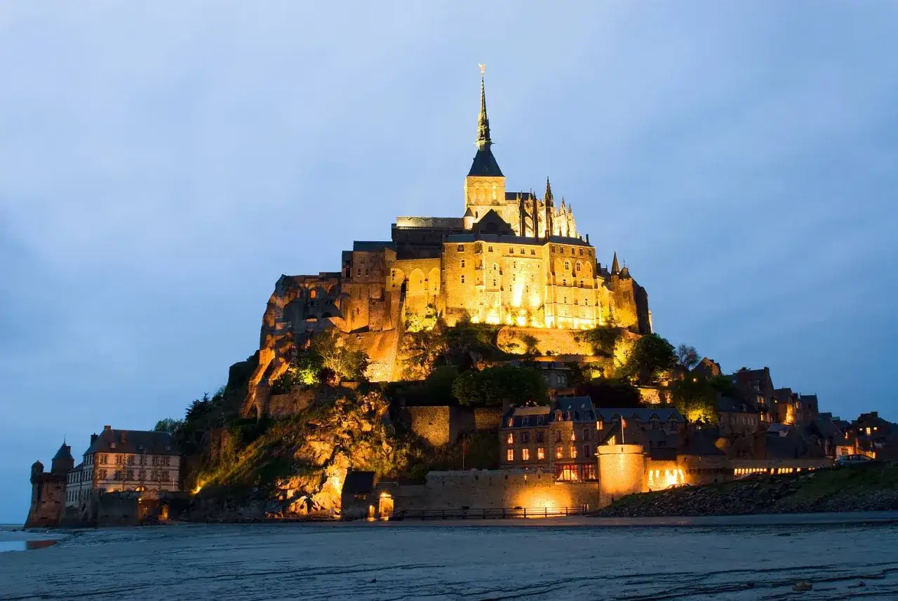 Mont Saint-Michel, symbol z czego słynie Francja, nocą, oświetlony, na tle nieba.
