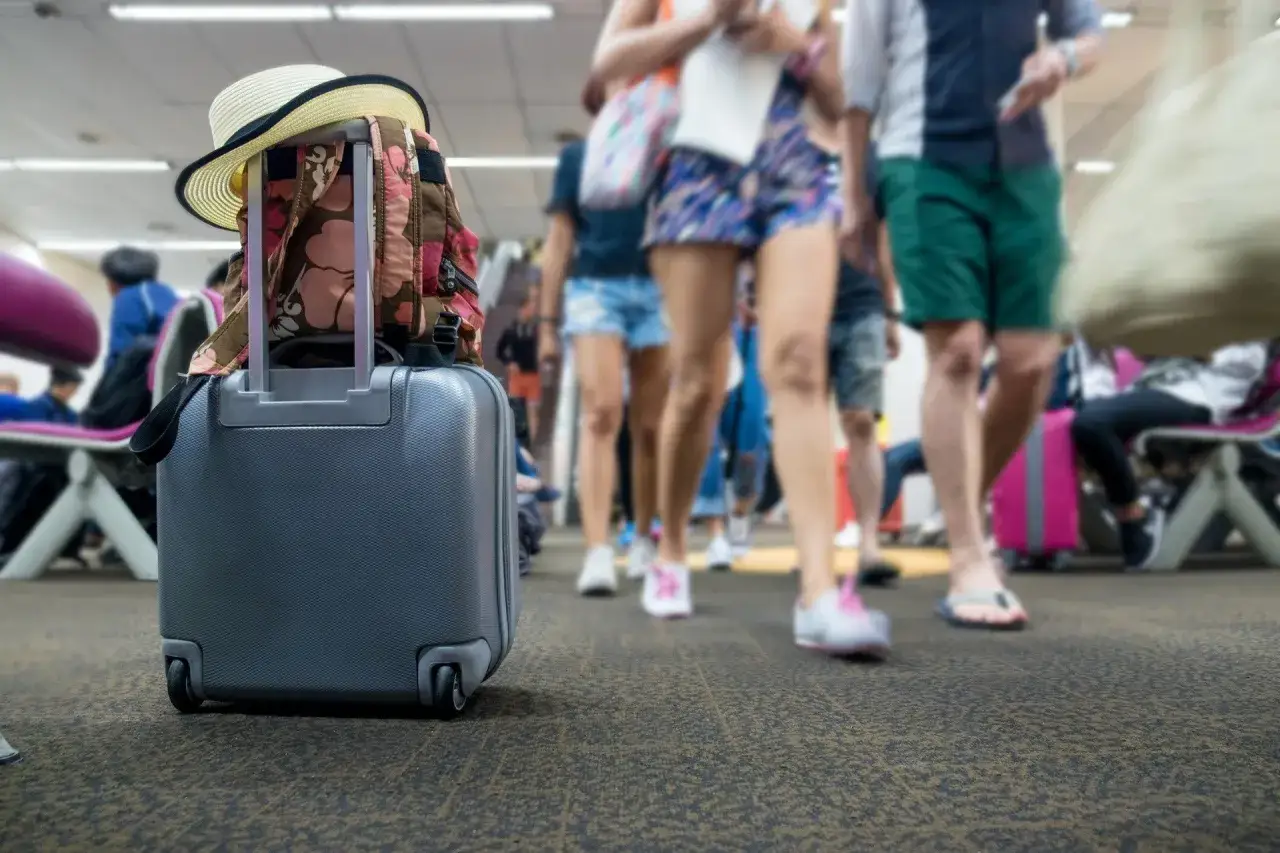 Walizka z plecakiem i kapeluszem na lotnisku. Ludzie w tle spieszą się na samolot, a Ty zastanawiasz się, co to turystyczny fundusz gwarancyjny.