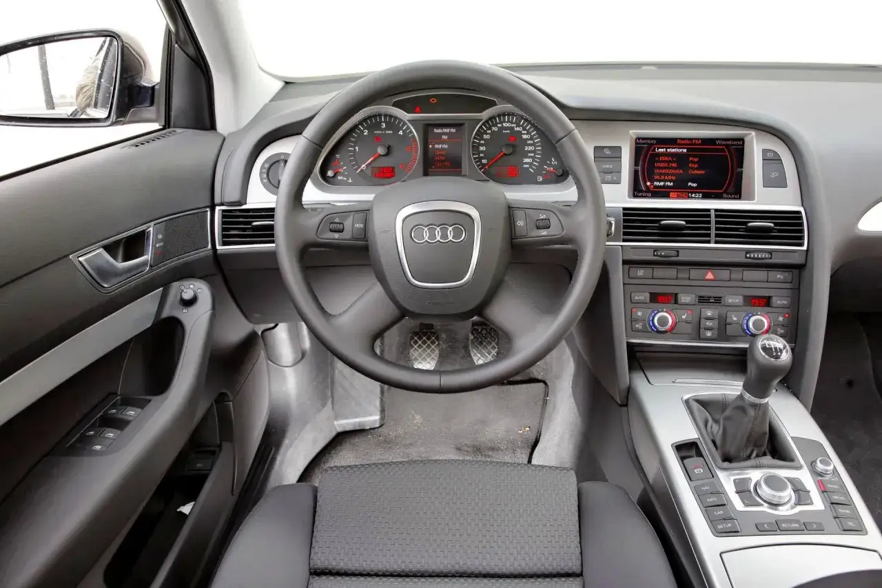 Wnętrze Audi A6 C6: kierownica, deska rozdzielcza z ekranem multimediów i zegarami, dźwignia zmiany biegów.