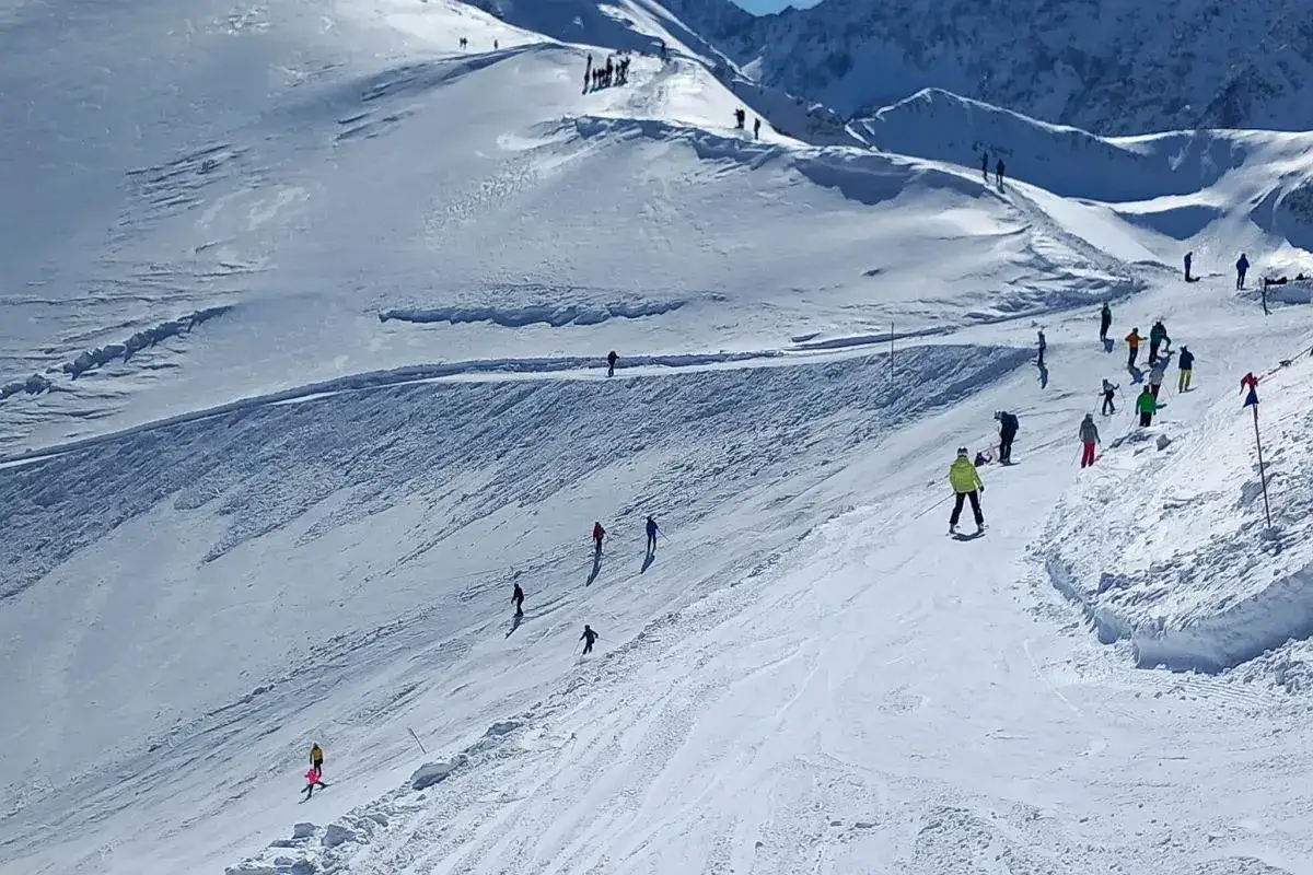 Narciarze szusują po ośnieżonych zboczach Kasprowego Wierchu. Widoczne są przygotowane trasy zjazdowe i grupy ludzi cieszące się zimowym krajobrazem.