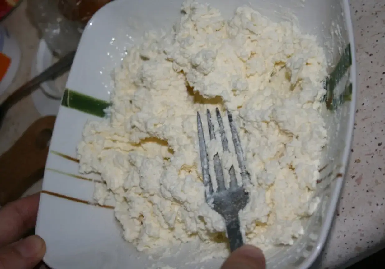 Twaróg w misce, gotowy do przygotowania pysznego obiadu. Widok na widelca mieszającego ser.