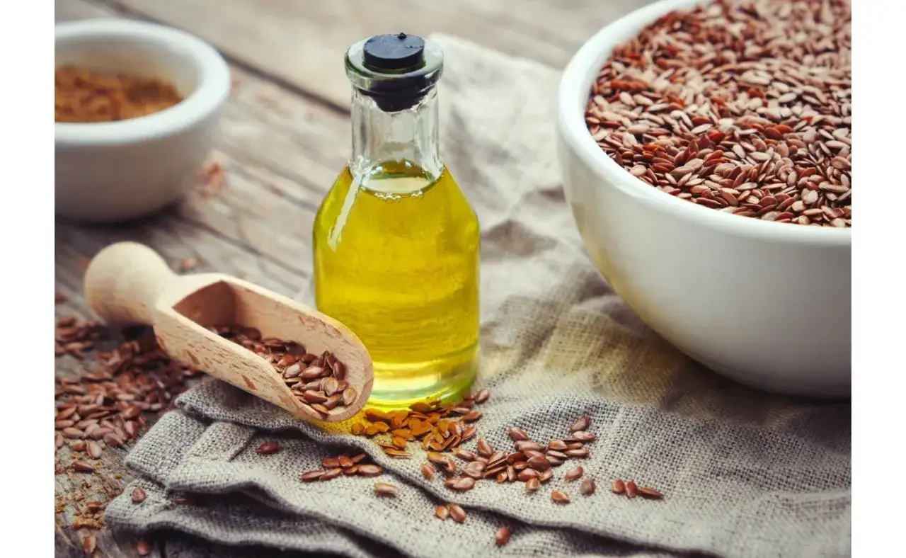 Butelka oleju lnianego, miska z nasionami lnu i drewniana łyżka. Odkryj niezwykłe olej lniany właściwości.