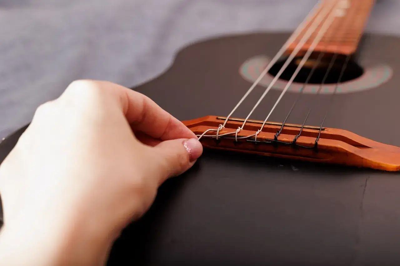 Dłoń poprawia struny w gitarze, przygotowując instrument do gry.
