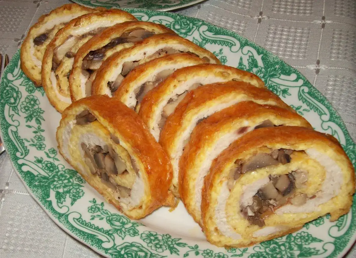 Roladki z kurczaka z pieczarkami i serem z piekarnika, pokrojone w plastry, prezentują się apetycznie na zielono-białym talerzu.
