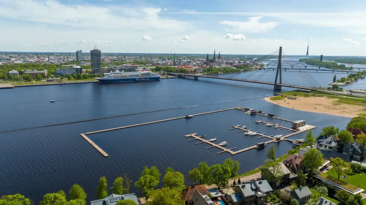 Widok na rzekę w Rydze, gdzie cumuje statek wycieczkowy. Miasto z mostami i wieżowcami. Czy Łotwa ma dostęp do morza? Tak, przez Zatokę Ryską.