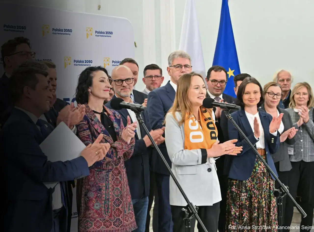 Kobieta w pomarańczowej szarfie przemawia, obok inni politycy. Podsumowanie obietnic wyborczych Polska 2050 co udało się zrealizować.