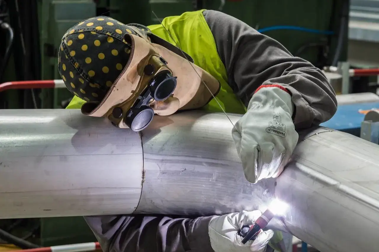 Spawacz w charakterystycznym czepku spawalniczym i goglach precyzyjnie łączy metalowe elementy.
