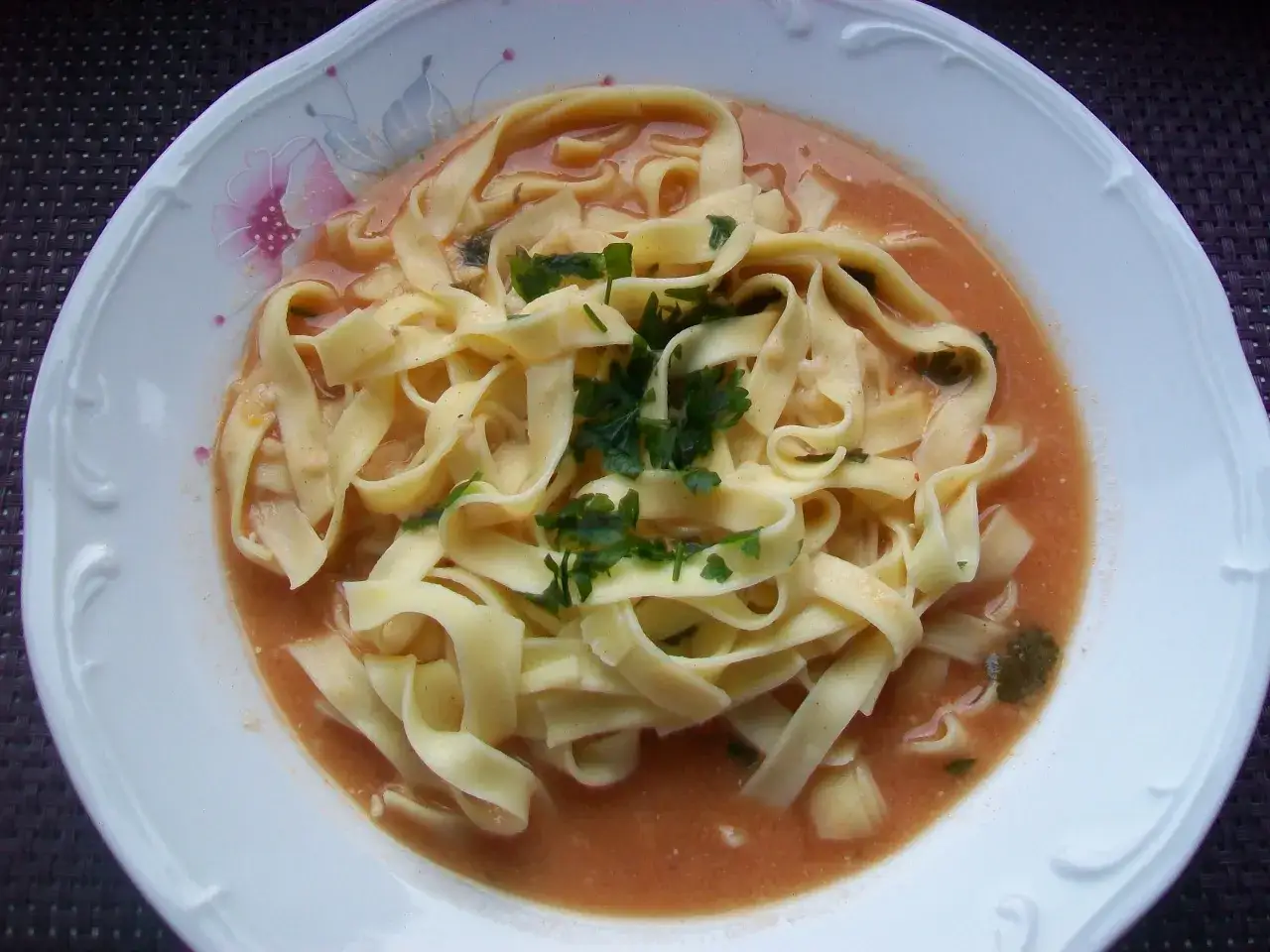 Talerz z makaronem w sosie pomidorowym, posypany natką pietruszki. Idealny sposób, jak podbić zupę pomidorową, dodając do niej pyszny makaron.