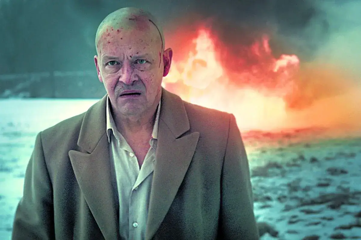 Jan Frycz w dramatycznym kadrze, przypominającym scenę z jego filmów i seriali. W tle płomienie, na twarzy niepokój.