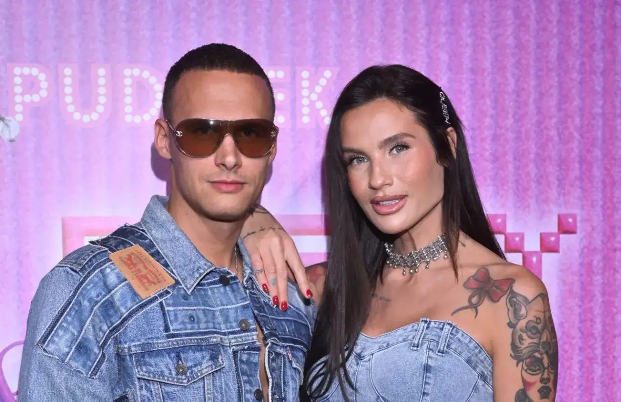 Mateusz Świerczyński z Love Island w dżinsowej kurtce i jego partnerka na tle r&oacute;żowej ściany.