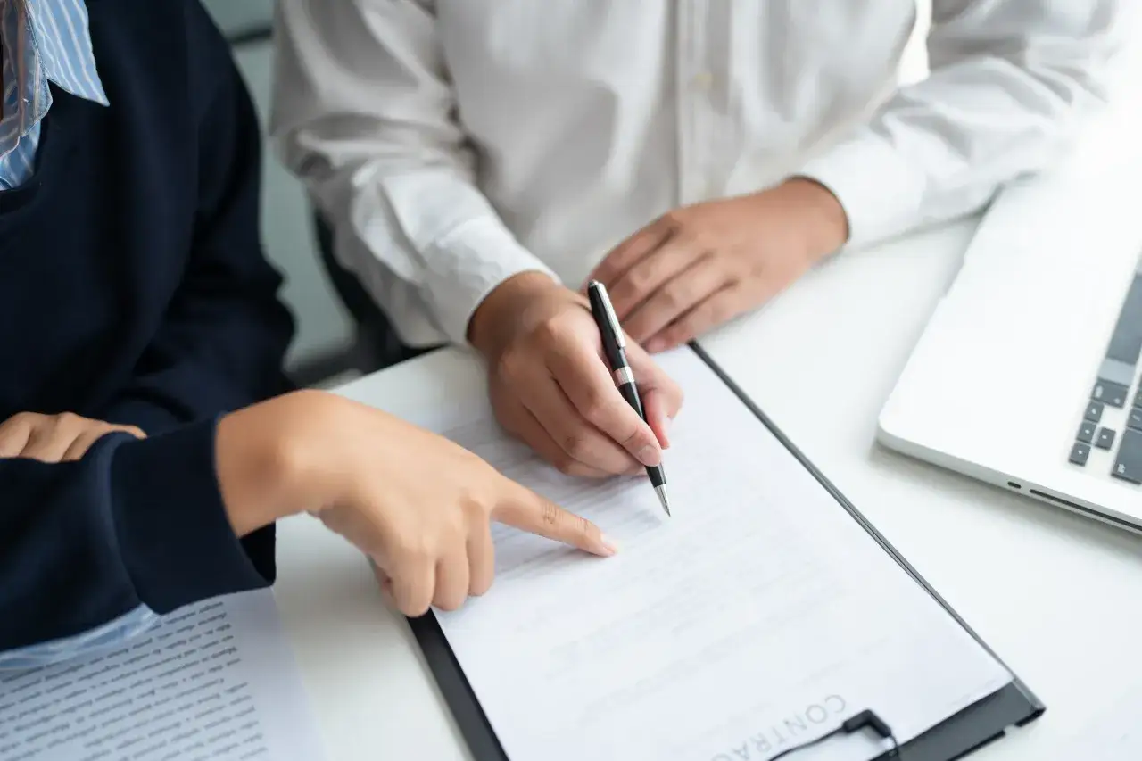 Dwie osoby przy biurku podpisują dokument. Dowiedz się, jak sprawdzić, czy notariusz jest prawdziwy, zanim złożysz podpis.