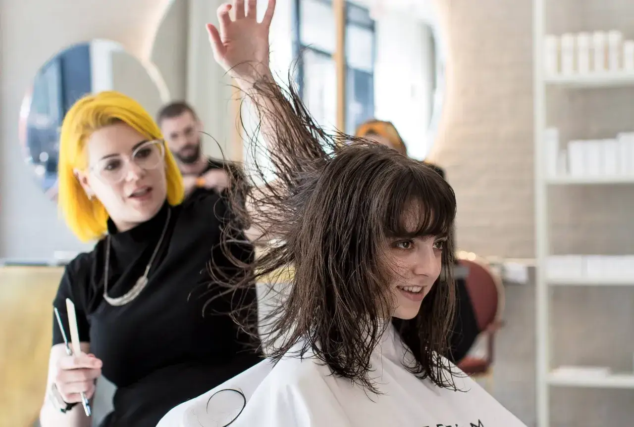 Fryzjerka z ż&oacute;łtymi włosami modeluje mokre, proste włosy klientki.