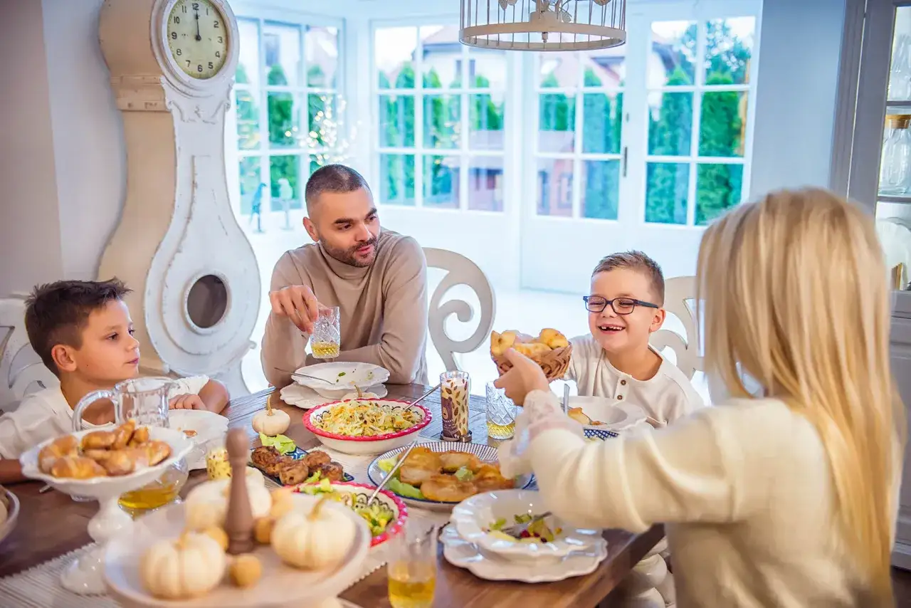 Rodzice z dzieckiem przy stole, świętują rodzinny obiad. Wszyscy uśmiechnięci, cieszą się wspólnym posiłkiem.