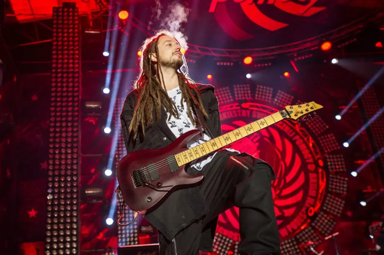 Baron z dredami gra na gitarze na scenie, z dymem unoszącym się z jego ust.
