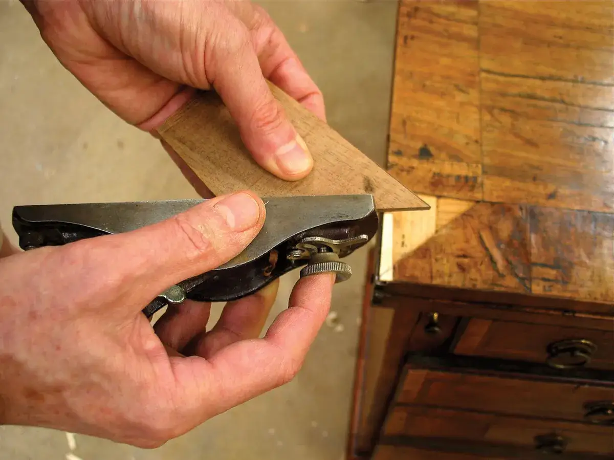 Ręce dopasowują fornir za pomocą małego strugarka. To kluczowy etap, by wiedzieć, czym pomalować fornir, aby efekt był idealny.