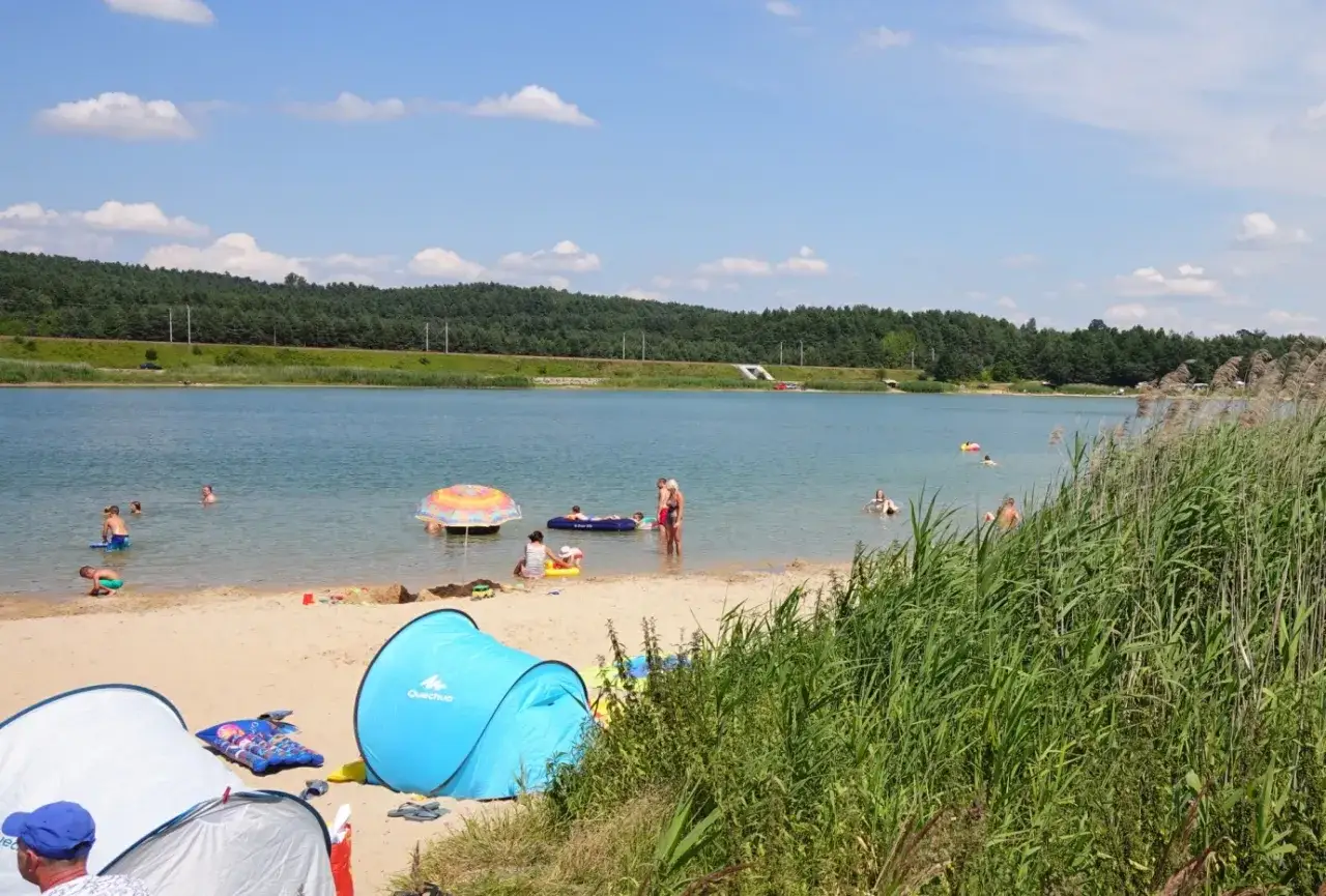 Słoneczny dzień nad zalewem Dźibice. Ludzie kąpią się, pływają na materacach i odpoczywają na plaży pod namiotami.