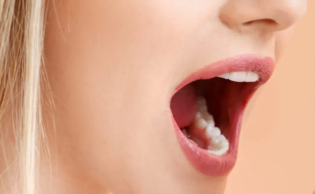 Usta otwarte, widoczne zęby i język. Może to być objaw b&oacute;lu podniebienia przy zębach g&oacute;rnych, kt&oacute;ry utrudnia m&oacute;wienie.