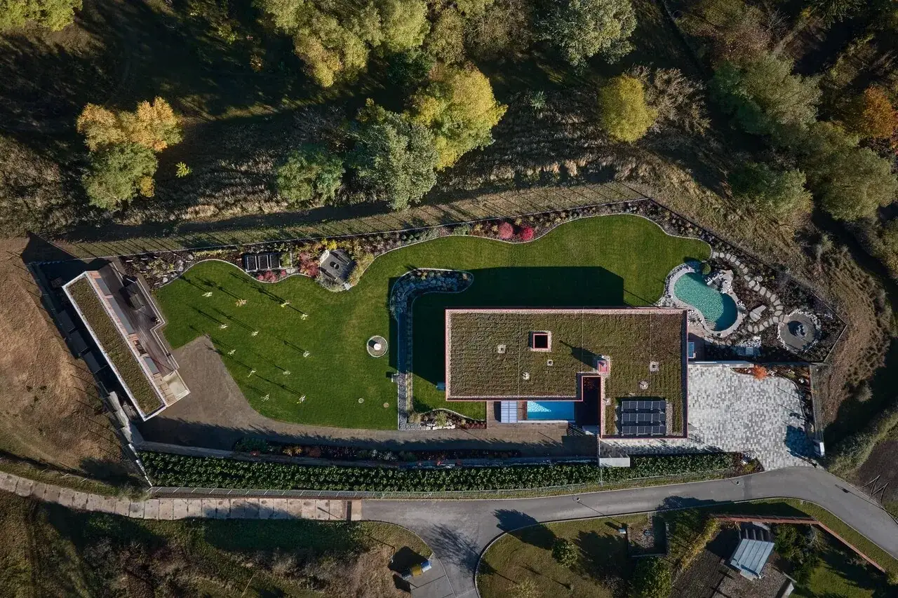 Nowoczesny dom z zielonym, **dachem płaskim** i basenem, otoczony ogrodem i lasem.