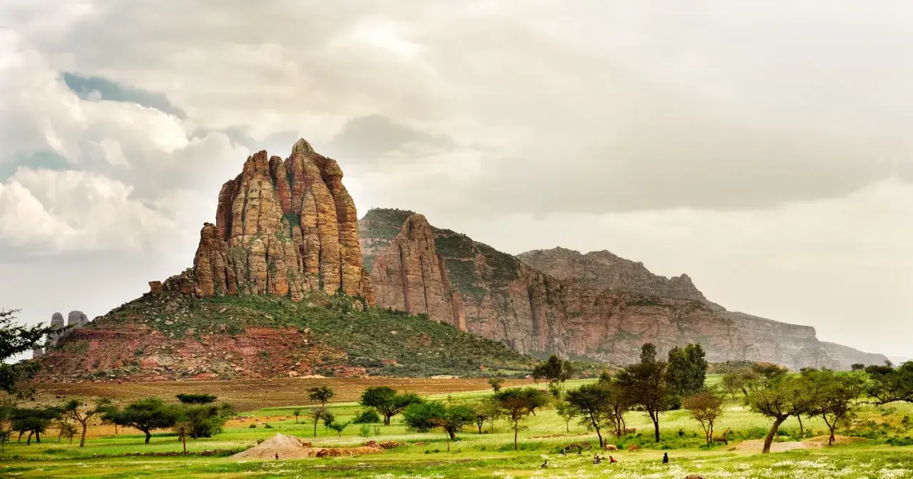 Etiopia miasto: majestatyczne g&oacute;ry skalne wznoszą się nad zieloną doliną z drzewami i ludźmi.